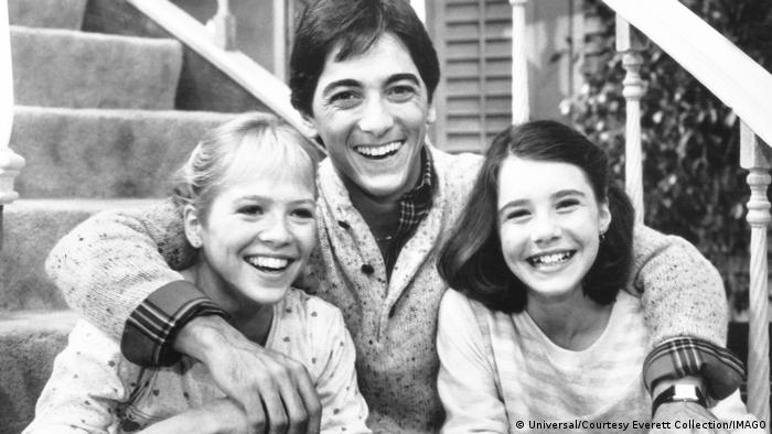 Black and white picture of two girls and a man in the middle smiling at the camera