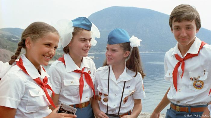 Picture of three girls and a boy dressed in uniforms with a lake and a mountain in the background