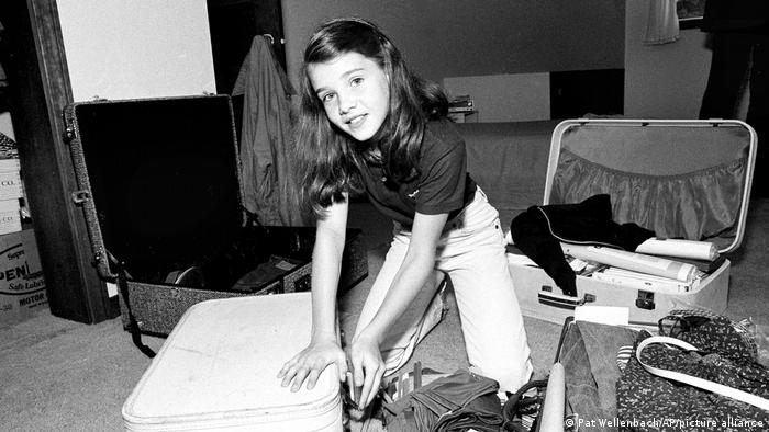 Black and white picture of a dark haired young packing while surrounded by suitcases