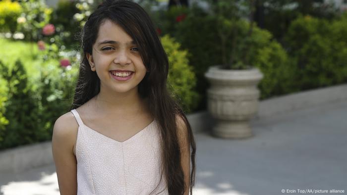 A young girl with long dark hair smiles at the camera