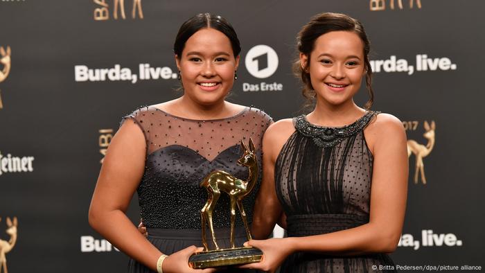 Two young ladies hold an award in the shape of a golden deer smile at the camera 