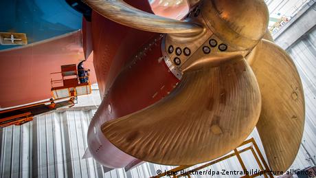 Die riesige bronzefarbene Schiffsschraube der „Global Dream“, im Hintergrund Menschen auf einer Hebebühne