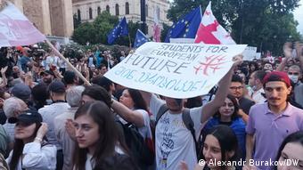 Участник демонстрации в Тбилиси держит плакат с надписью Студенты за европейскоу будущее и флагом Грузии