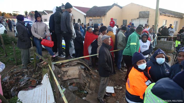 Crowd gathers as forensic personnel investigate after the deaths of patrons found inside the Enyobeni Tavern