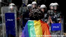 TOPSHOT - A participant faces riot policemen wearing a rainbow flag during a Pride march in Istanbul, on June 26, 2022. - Turkish police forcibly intervened in a Pride march in Istanbul, detaining dozens of demonstrators and an AFP photographer, AFP journalists on the ground said. The governor's office had banned the march around Taksim Square in the heart of Istanbul but protesters gathered nearby under heavy police presence earlier than scheduled. (Photo by KEMAL ASLAN / AFP) (Photo by KEMAL ASLAN/AFP via Getty Images)