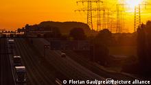 Symbolbild Energie: Sonnenaufgang über der A5 bei Frankfurt am Main mit Hochspannungsleitungen im Hintergrund