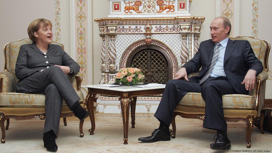 Merkel e Putin sentados em sala com adornos luxuosos