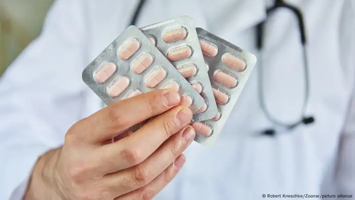 A white, male doctor's hand holding pill sleeves