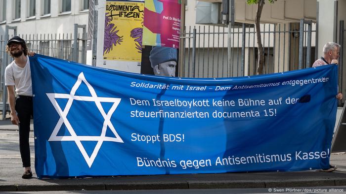 Protestierende halten ein blaues Banner hoch auf dem steht: Solidarität mit Israel - Dem Antisemitismus entgegentreten. Dem Israelboykott keine Bühne af der steuerfinanzierten documenta 15! Stoppt BDS! Bündnis gegen Antisemitismus Kasse!