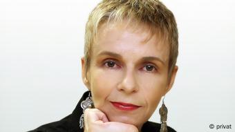 Close-up of a woman with short blonde hair and brown eyes, wearing red lipstick and dangly earrings