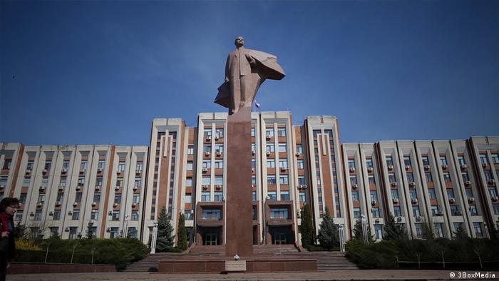 Überlebensgroßes Lenin-Denkmal auf einer Säule vor einem großen Gebäusekomplex