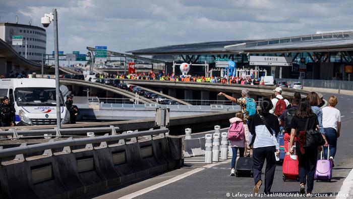 Travelers arrive on foot at Roissy-Charles de Gaulle airport while airport workers demonstrate