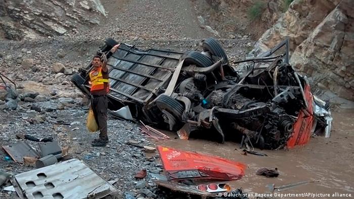 A rescue worker stands next to the wreckage of a passenger bus, in Zhob, Baluchistan province, in southwestern Pakistan