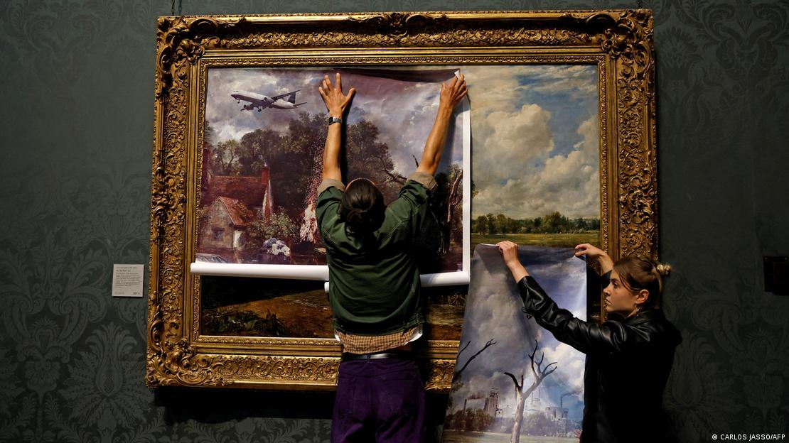 Um homem e uma mulher colam uma nova imagem sobre uma obra de arte. 