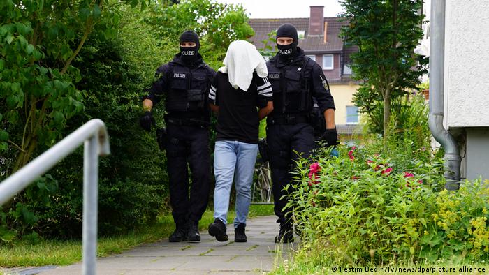Deux policiers allemands escortent un suspect arrêté, qui a une serviette sur la tête pour masquer son identité, à Osnabrück le 5 juillet 2022. 
