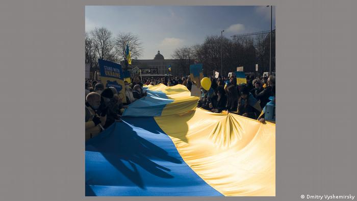 Demonstrierende halten eine riesige, blaugelbe ukrainische Fahne.