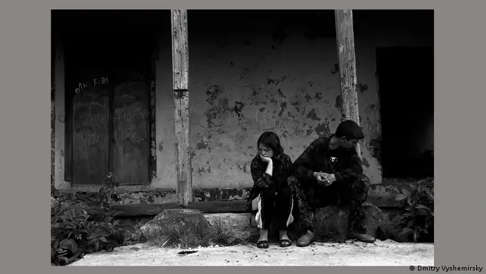 Schwarz-weiß-Foto eines jungen Mannes und einer jungen Frau, die vor einer Hausruine sitzen.