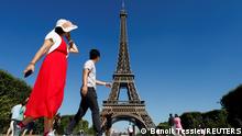 Tourists walk in front of the Eiffel tower during the 20th campaign of painting and stripping in Paris, France, July 5, 2022. REUTERS/Benoit Tessier