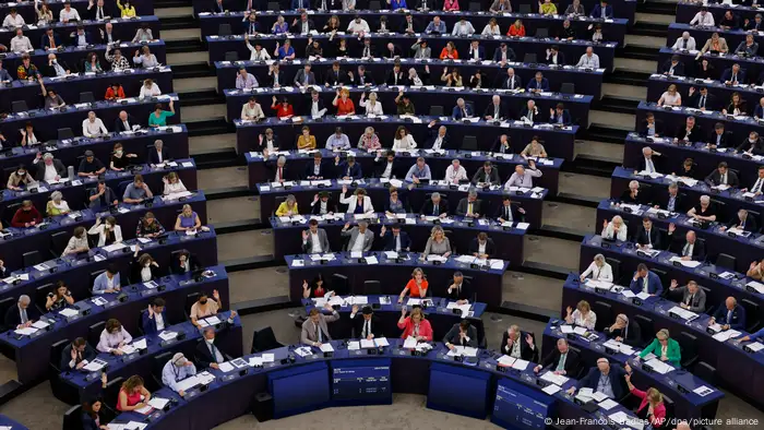 Blick in einen vollbesetzten Plenarsaal mit blauen Stühlen und vielen Abgeordneten, die teilweise ihre Hand zur Abstimmung heben