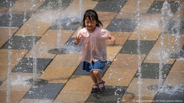 Une fille traverse une fontaine dans un quartier commerçant en plein air lors d'une journée exceptionnellement chaude à Pékin
