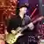 Carlos Santana steht mit einer goldenen Gitarre auf der Bühne, trägt einen schwarzen Pullover und einen schwarzen Hut.
