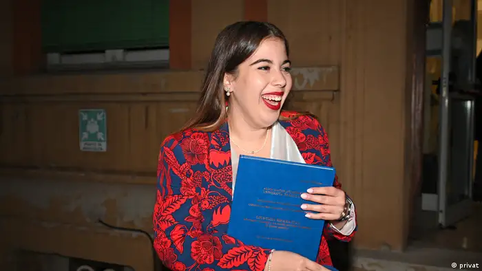 Junge Frau mit rotem Jackett hält ein Zeugnis in der Hand und lacht fröhlich 
