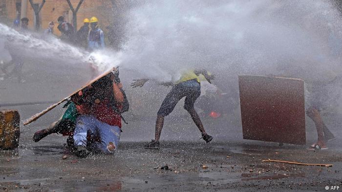 Sudanese anti-coup protesters take cover as riot police try to disperse them with a water cannon
