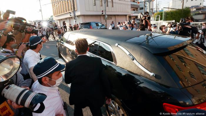 A black hearse drives through a crowd of journalists