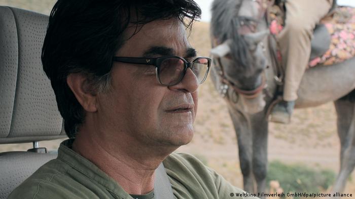 Jafar Panahi sitzt in seinem Film Drei Gesichter in einem Auto am Steuer. Im Hintergrund ist ein Pferd mit Reiter zu sehen. 