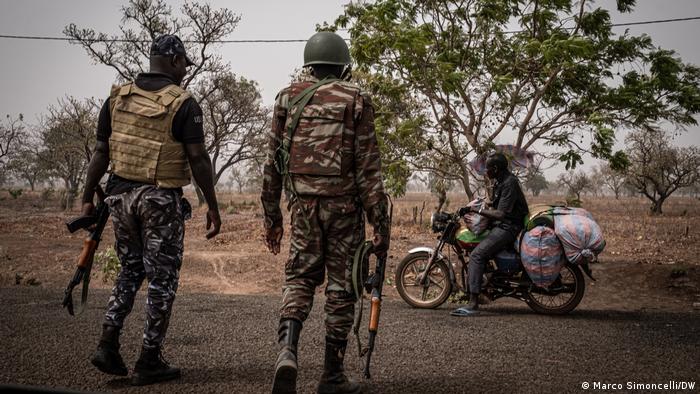 Two armed soldiers speak with a man on a motorcycle at a checkpoint near Porga