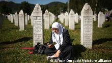 A Bosnian muslim woman prays at a grave in Memorial Centre in Potocari, Monday, July 11, 2022. Thousands converge on the eastern Bosnian town of Srebrenica to commemorate the 27th anniversary on Monday of Europe's only acknowledged genocide since World War II. (AP Photo/Armin Durgut)