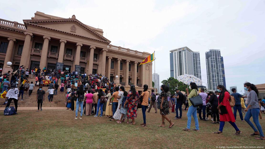 Multidão faz fila diante de edifício em estilo neoclássico