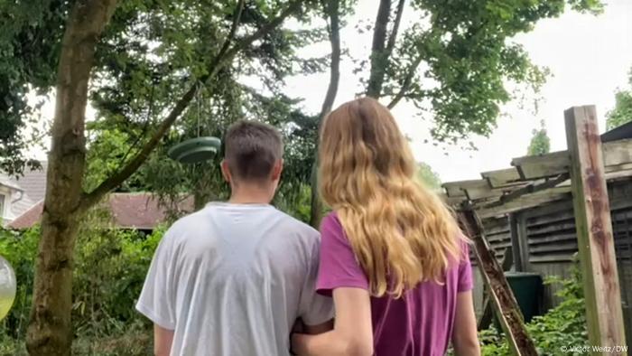 Anna and Alex, a same-sex couple from Odessa as seen from behind, one with short hair the other long, both in t-shirts, before a green urban landscape