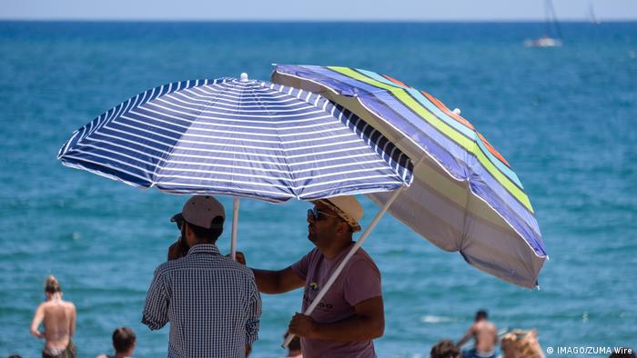 Two men under umbrellas by the sea in Barcelona