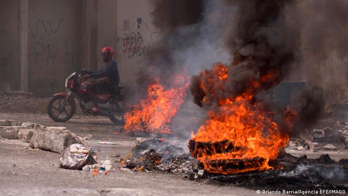 A man on a motorcycle passes burning barricades