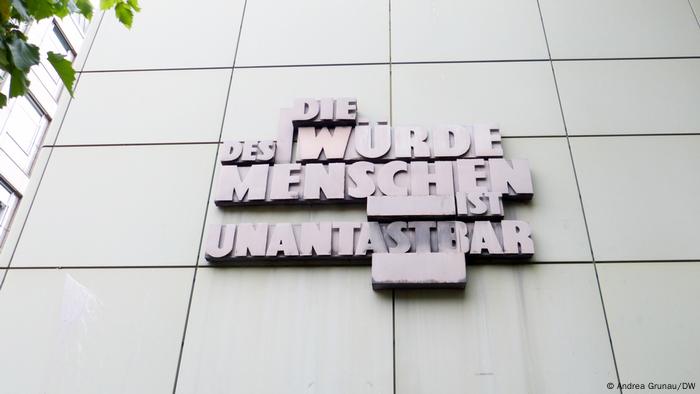 Ein rotes Schriftrelief prangt auf einer grauen Gebäudefront: Die Würde des Menschen ist unantastbar Ein rotes Schriftrelief prangt auf einer grauen Gebäudefront: Die Würde des Menschen ist unantastbar