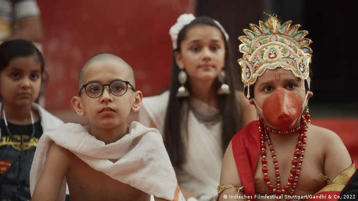 Photo tirée de 'Gandhi & Co' : 4 enfants regardent attentivement quelque chose devant eux, l'un porte une couronne, un masque orange et un collier de perles rouges, l'autre porte un costume rappelant Gandhi. 