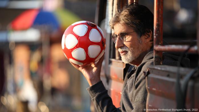 Amitabh Bachchan dans une photo de 'Jhund' : un homme tient un ballon de football rouge et blanc.