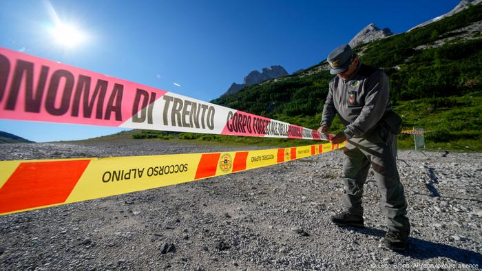 An Italian police officer inspects a cordon; mountains are visible behind him