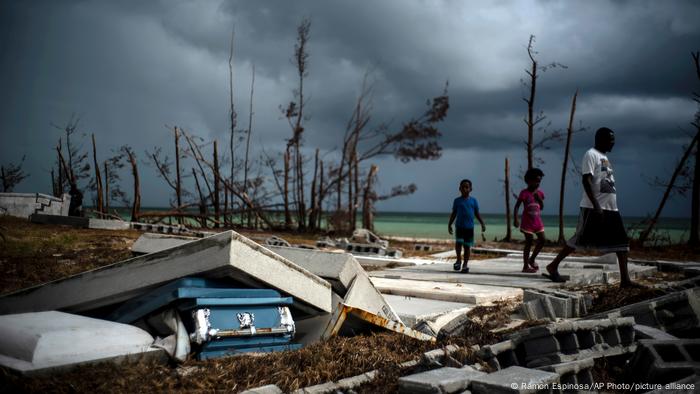 People walk next to a shattered and water-filled coffin lying next to debris after Hurricane Dorian hit the Bahamas 