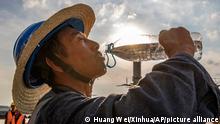 China: Ein Mann mit Strohhut trinkt Wasser, im Hintergrund die gleißende Sonne