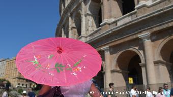 A tourists holds a paper umbrella to protect herself from the sun near the Colosseum in Rome