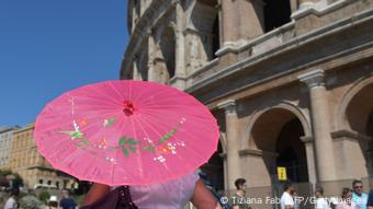 A tourists holds a paper umbrella to protect herself from the sun near the Colosseum in Rome