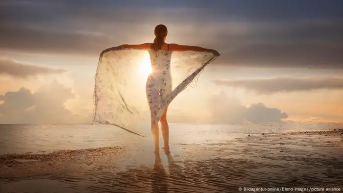 Caucasian woman holding fabric on beach at sunset
