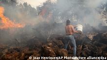 Ein Anwohner versucht mit Wasser aus einem Eimer die Flammen eines Waldbrandes zu löschen. Das im Sommer von Waldbränden bislang weitgehend verschonte Portugal wird nun von einer Hitzewelle und Dutzenden von Feuern heimgesucht. +++ dpa-Bildfunk +++