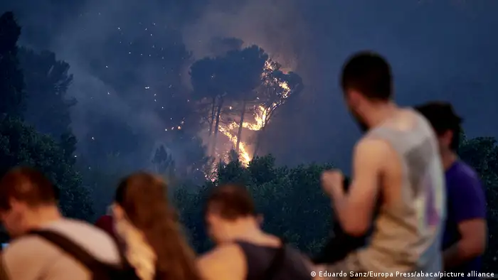Evacuated residents look on as fire ravages a forest in Spain