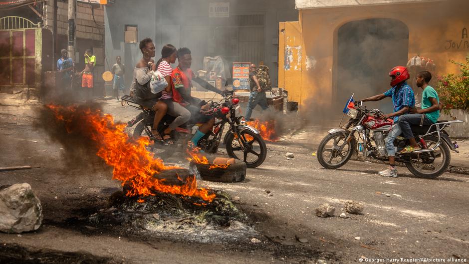 Men on motorbikes riding through the fire in a street in Haiti.