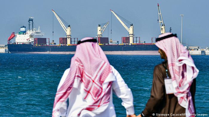 Zwei in arabische Gewänder gekleidete Männer blicken im Hafen von Ras al-Khair auf einen Öltanker