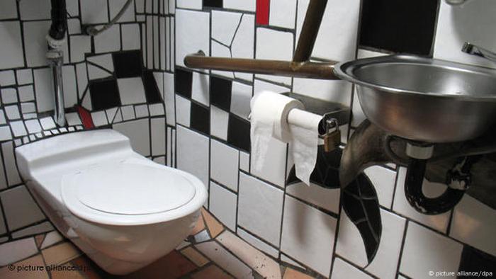 Toilet in a bathroom with white broekn tiles and crooked walls