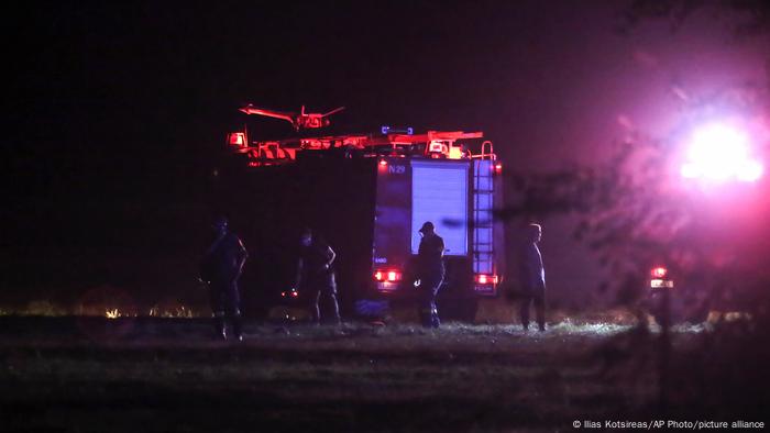 Firefighters stand around a truck in the night as a round, bright object shines from the righthand night sky